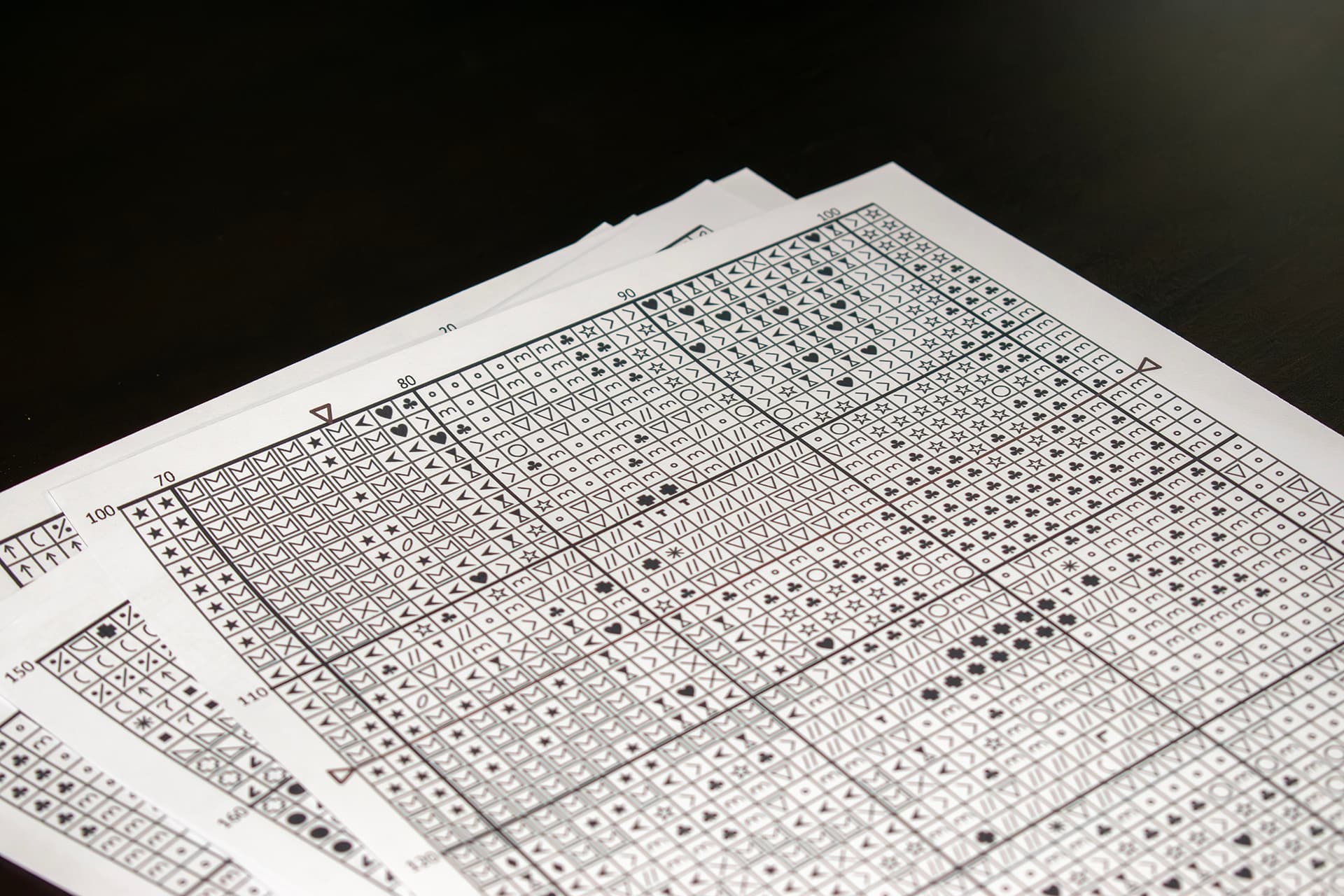 Printed cross-stitch charts fanned out, every square carrying the symbol of one thread shade